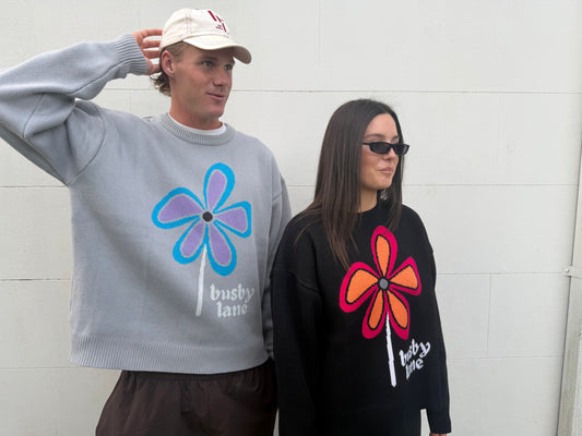 Two models wearing oversized crewneck sweaters with large flower graphics and 'busby lane' text, standing against a white wall.